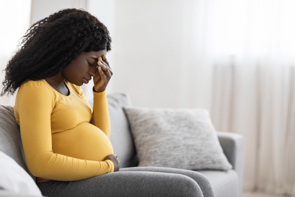 pregnant woman sitting on a couch and holding a hand to her head due to discomfort