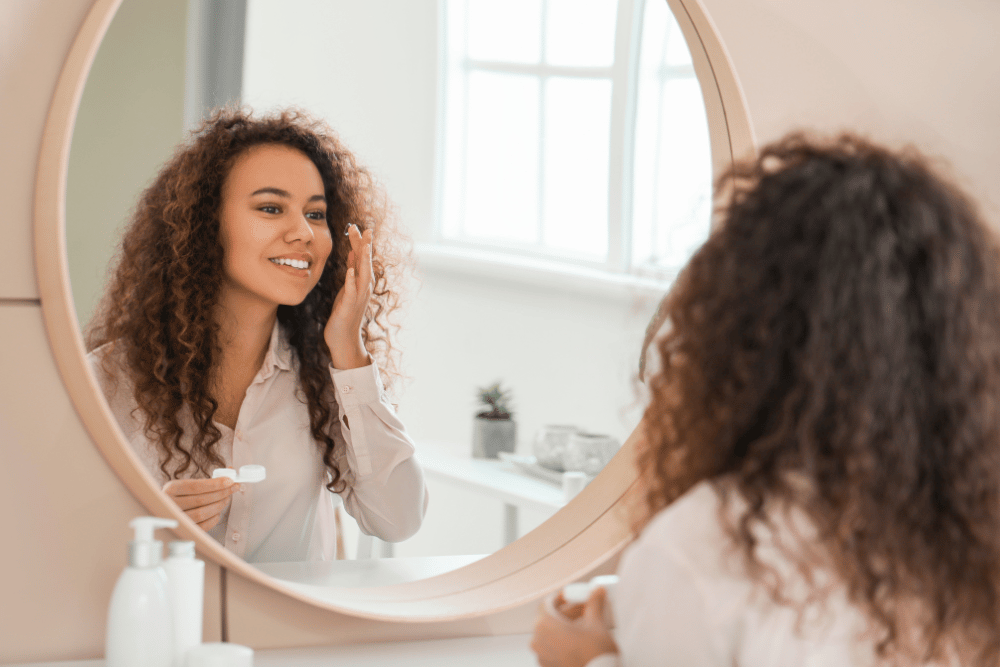 a young woman putting in contact lenses at home