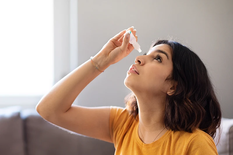a young woman putting in eye drops for dry eye