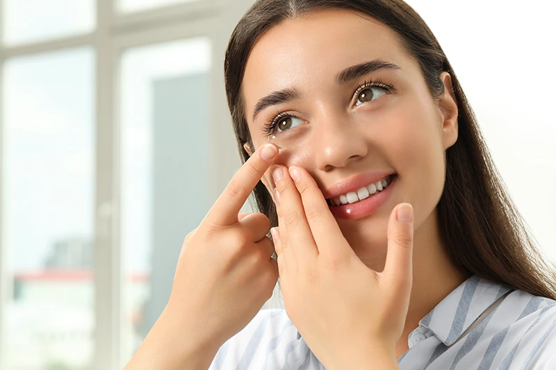 a smiling woman putting in a contact lens