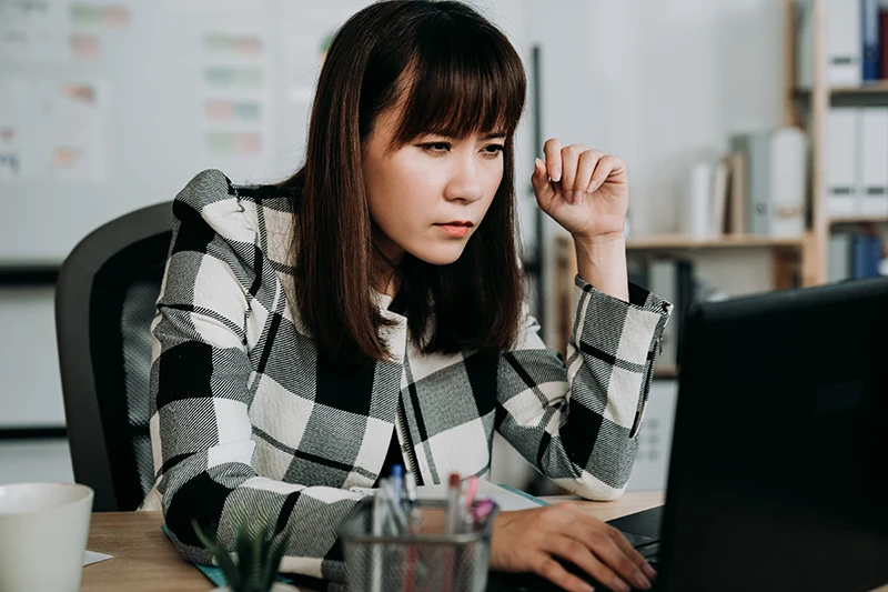 a young woman squinting while looking at computer at work
